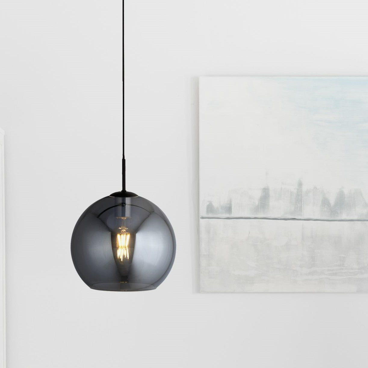 A dark glass pendant light illuminating a modern room with artwork in the background.