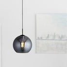 A dark glass pendant light illuminating a modern room with artwork in the background.