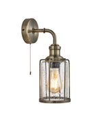 An antique brass wall light with a caged, seeded glass shade and a pull cord switch.