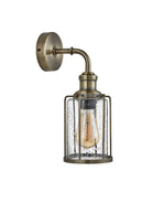 An antique brass wall light with a caged, seeded glass shade.