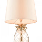 A close-up of the glass pineapple base, metal top, and cream shade of a table lamp.