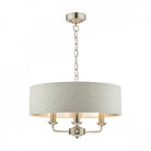 A stylish cream fabric drum shade chandelier with three gold candle-style lights hangs.
