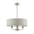 A modern cream fabric drum shade chandelier with three matte silver candle-style lights hangs.