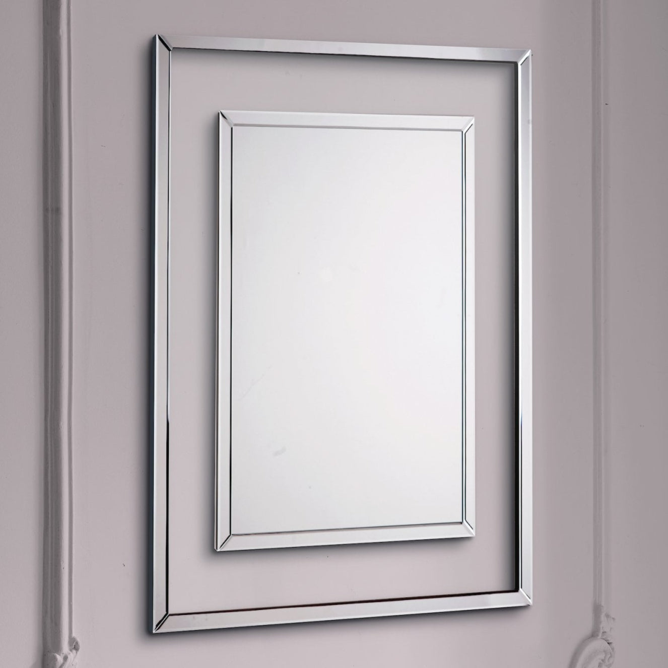 Ornate silver rectangular mirror with a smaller inner mirror, angled on a white wall.