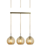 A close-up of three amber glass globe pendant lights hanging from a brass bar.