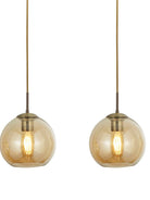 Two illuminated amber glass globe pendant lights with brass fittings on a white background.