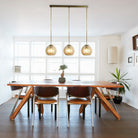 Three amber glass globe pendant lights hanging above a modern wooden dining table and chairs.