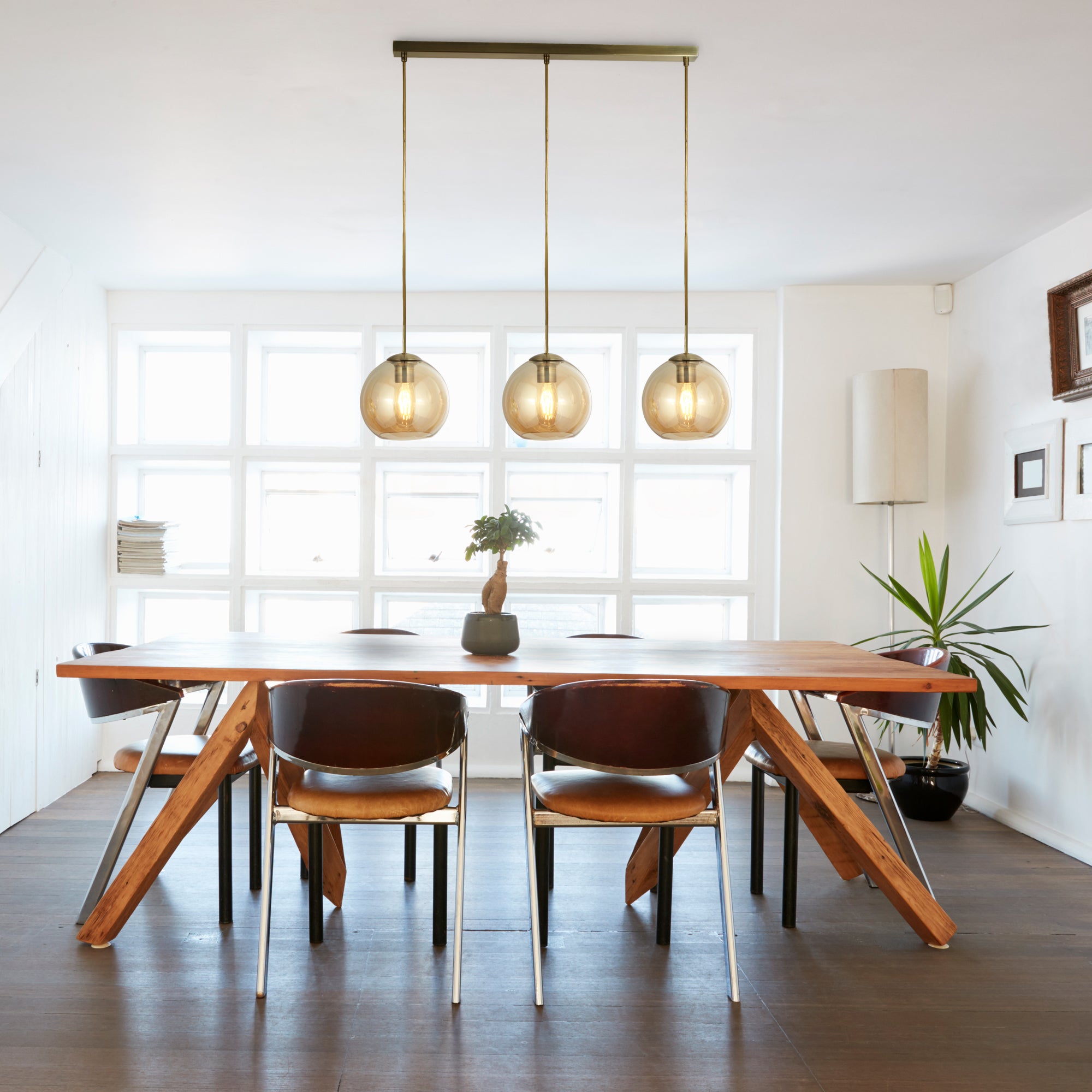 Three amber glass globe pendant lights hanging above a modern wooden dining table and chairs.