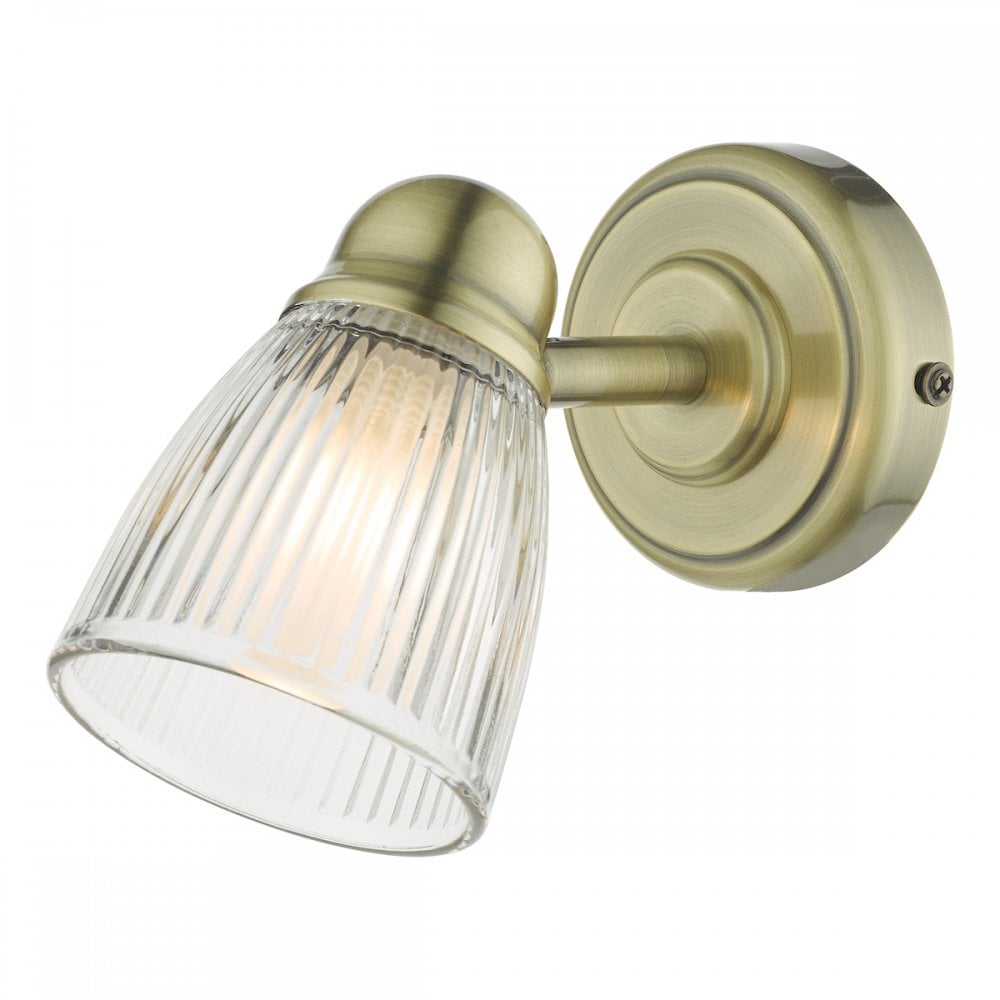 A brass wall light with a fluted glass shade, illuminated and casting a warm glow.