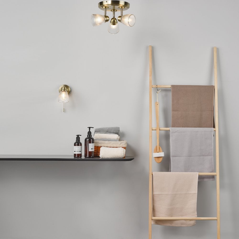 A bathroom setting with brass lighting fixtures, a wooden ladder, and neatly stacked towels.