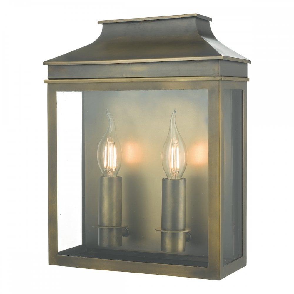 A brass outdoor wall lantern with two lit, candle-style bulbs inside its glass casing.