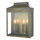 A brass outdoor wall lantern with two lit, candle-style bulbs inside its glass casing.