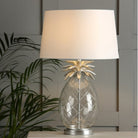 A pineapple-shaped table lamp with a white shade on a table in a dimly lit room.