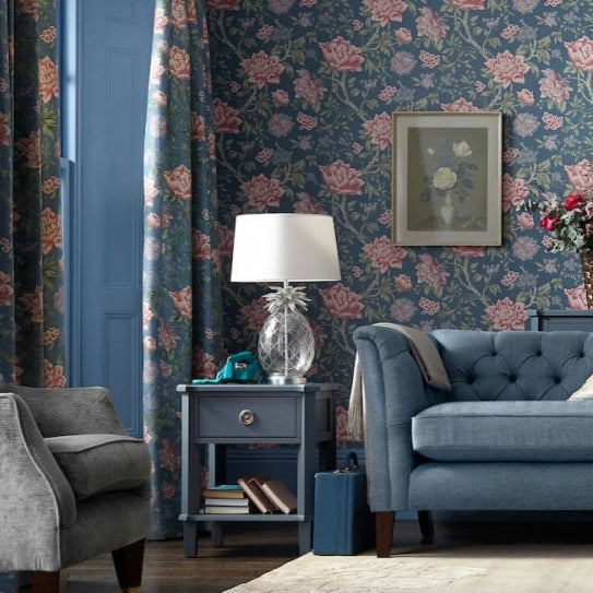 A living room with blue floral wallpaper, a blue sofa, and a pineapple-shaped lamp.