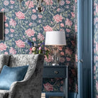 A living room with blue floral wallpaper, a grey armchair, and a blue side table with a lamp.