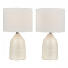 Two white ceramic table lamps with drum shades against a white background.