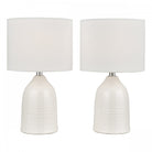 Two white ceramic table lamps with drum shades against a white background.