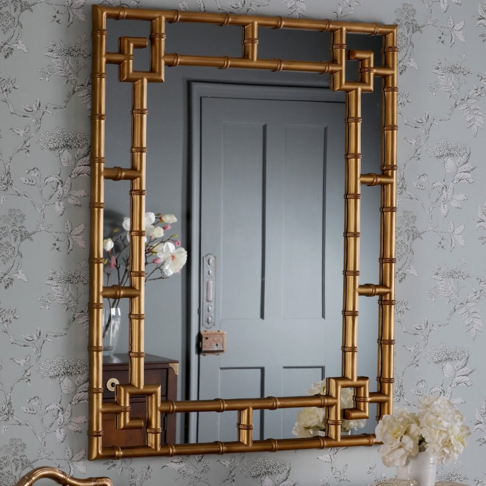 Ornate gold bamboo mirror reflecting a grey door and white flowers.