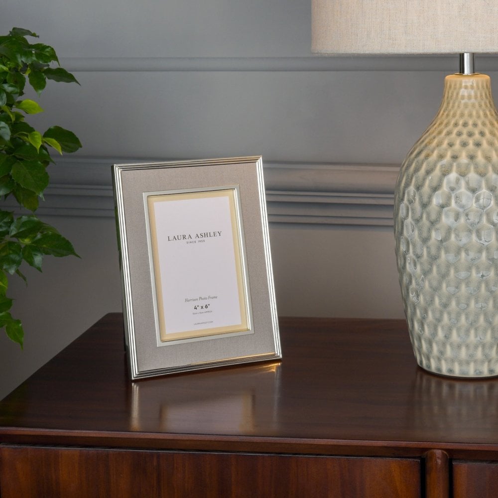 A 4x6 inch Laura Ashley photo frame, champagne colored, sits on a wooden dresser.