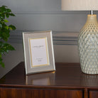 A 4x6 inch Laura Ashley photo frame, champagne colored, sits on a wooden dresser.