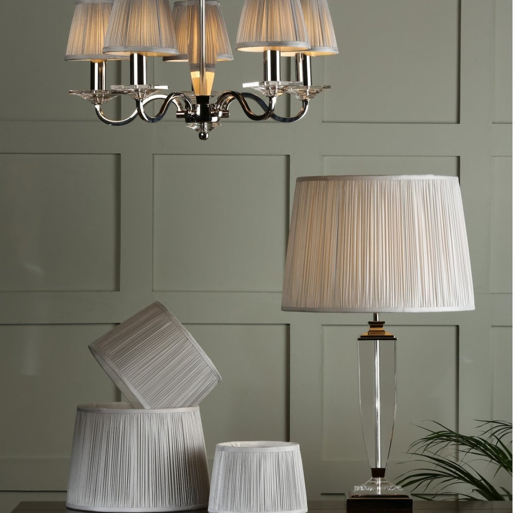 Pleated shades on a chandelier and a table lamp, with extra shades on the table.