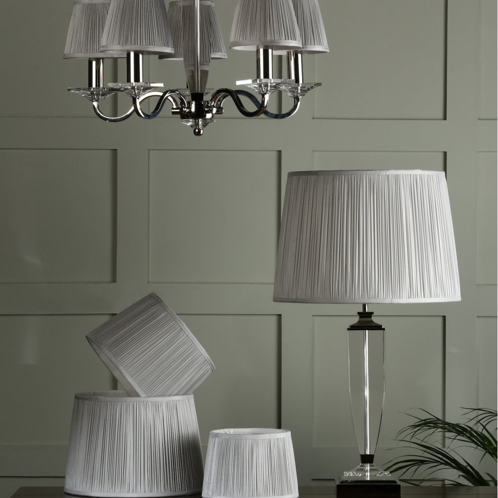 Pleated shades on a chandelier and a table lamp, with extra shades on the table.