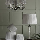 Pleated shades on a chandelier and a table lamp, with extra shades on the table.