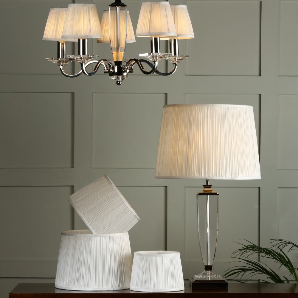 A pleated lampshade on a table lamp with matching lampshades on a chandelier.