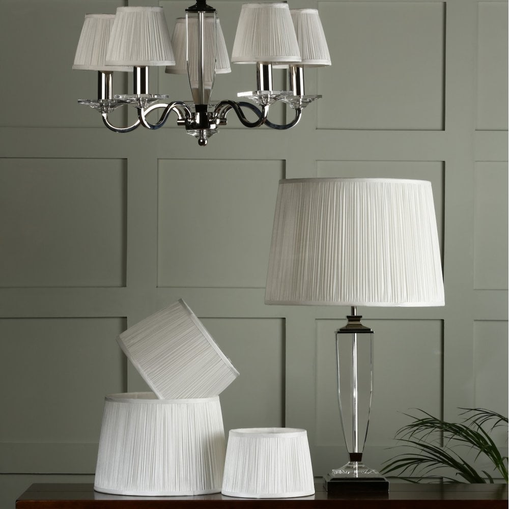 A pleated lampshade on a table lamp with matching lampshades on a chandelier.