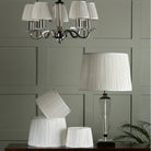 A pleated lampshade on a table lamp with matching lampshades on a chandelier.