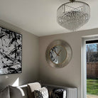 A contemporary living space with a dazzling crystal chandelier, modern art, and a large round mirror.