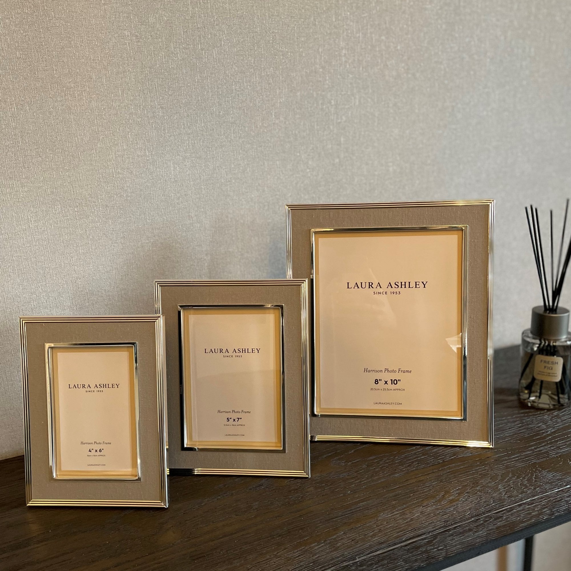 Three Laura Ashley photo frames in varying sizes and colors on a dark wooden surface.