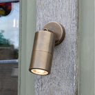 A brass wall light illuminates a wooden wall, providing ambient outdoor lighting.