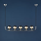 A linear pendant light with five smoky glass globes against a deep blue background.