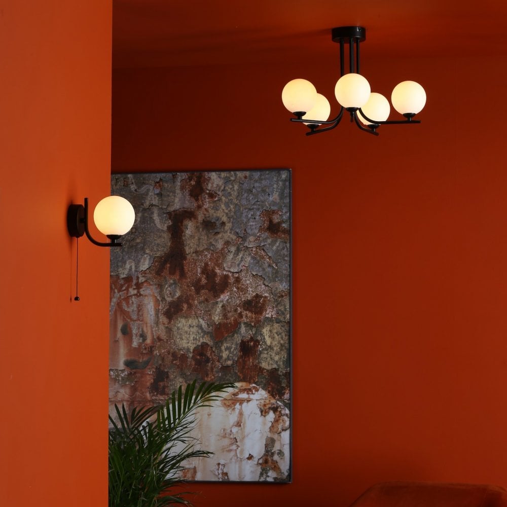 A ceiling light and a wall light with white spherical shades in a room with orange walls.