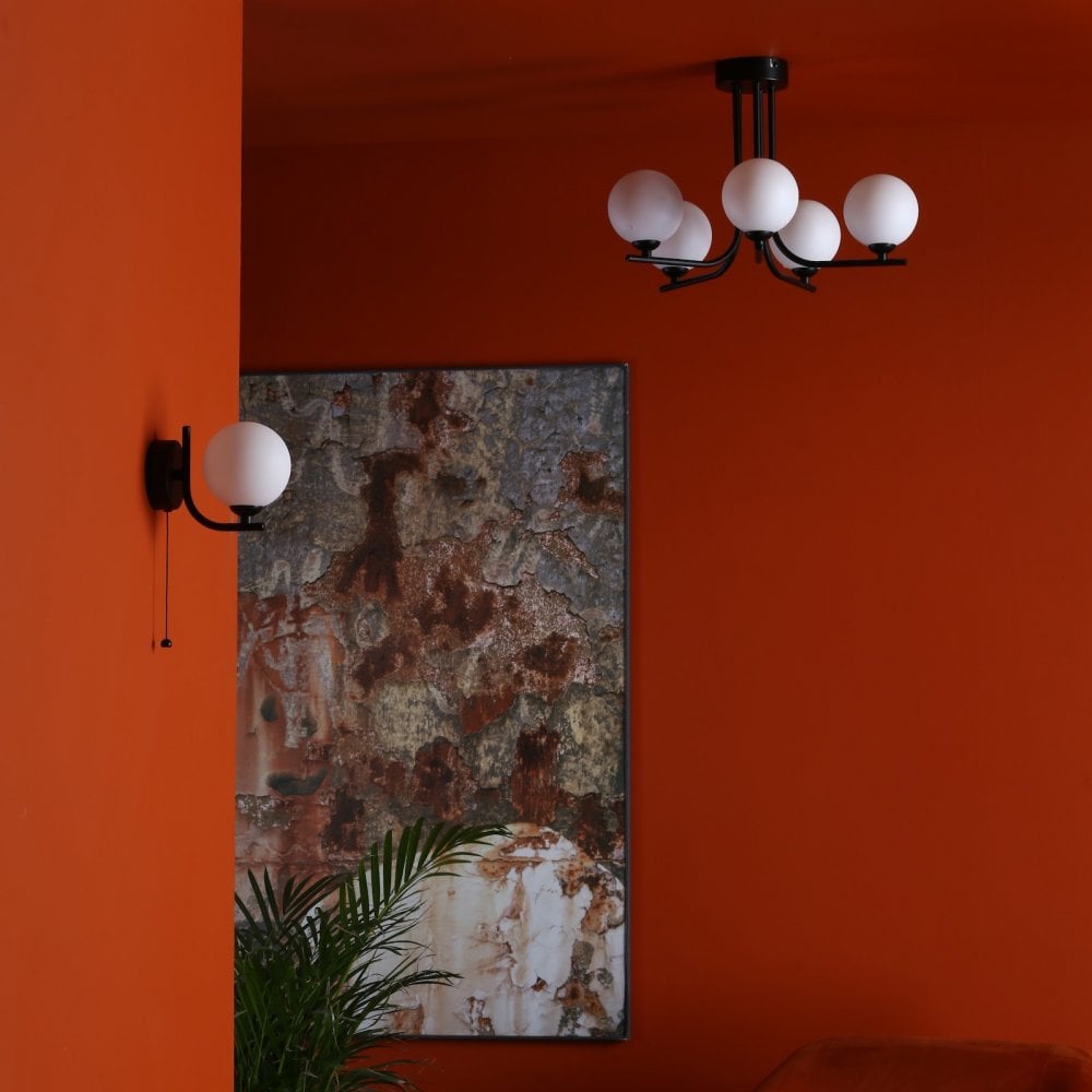 A ceiling light and a wall light with white spherical shades in a room with orange walls.