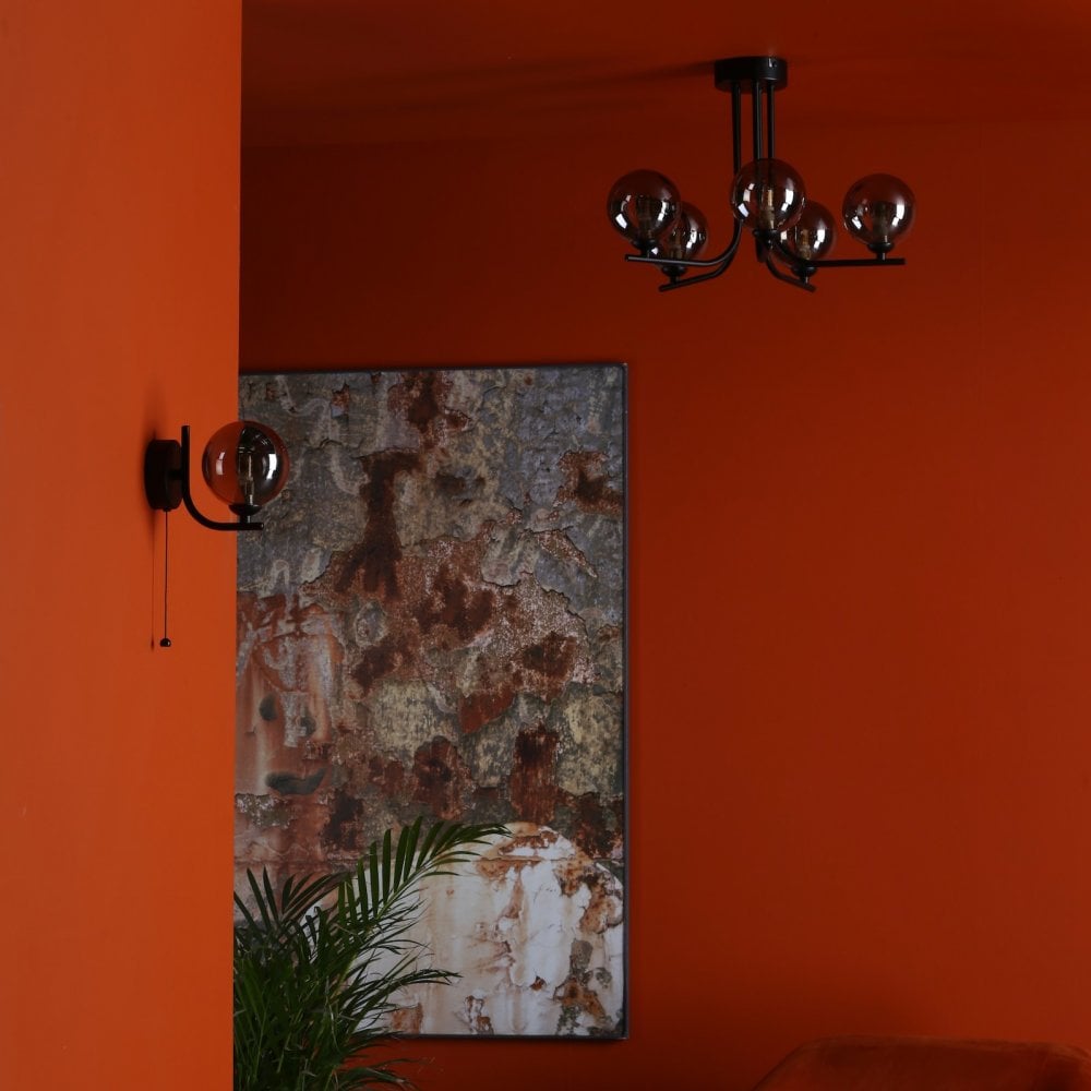 A modern orange room with a black chandelier and a coordinating wall sconce.
