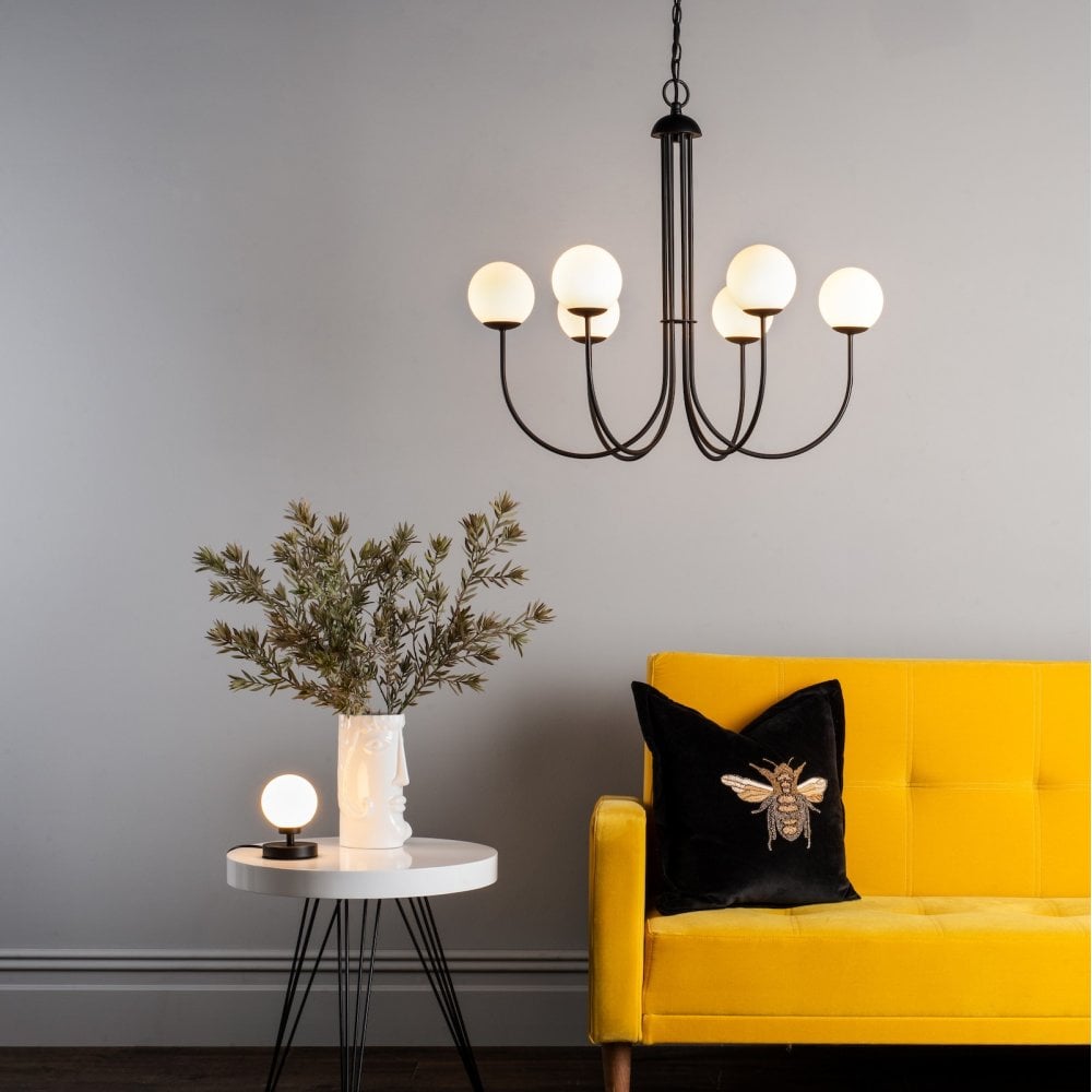 A modern living room with a yellow sofa, a spherical table lamp, and a chandelier.
