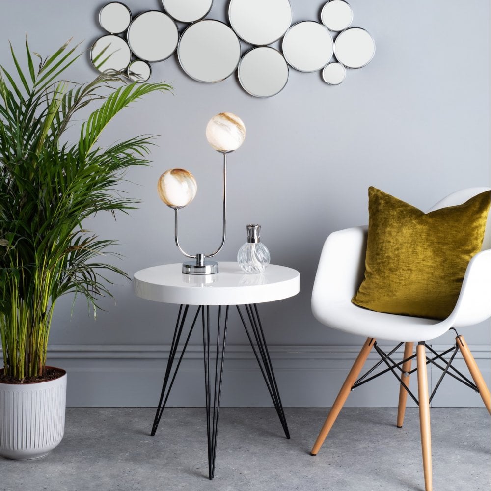 Table lamp with warm-toned shades on a white table in a room with a plant and chair.