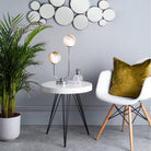 Table lamp with warm-toned shades on a white table in a room with a plant and chair.