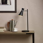 Black table lamp illuminating a desk with a coffee pot, cup, and books.