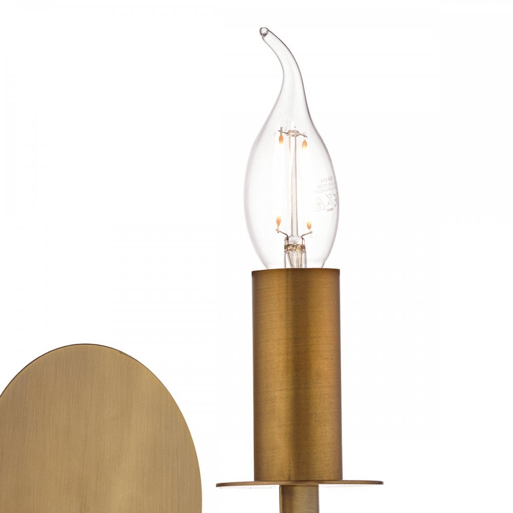 A close-up of the flame-shaped bulb and brass holder of a wall light.