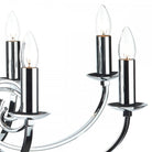 Close-up of three candle-shaped bulbs on the curved arms of a silver chandelier.