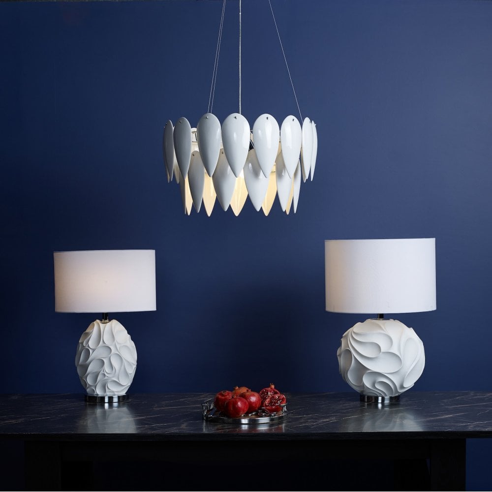 A white petal pendant light hangs above a console table with two white table lamps on a blue wall.