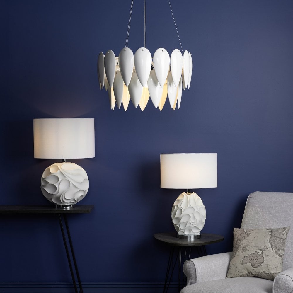 A white petal pendant light illuminates a room with a blue wall, two white lamps, and an armchair.