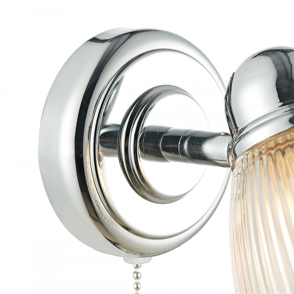 A close up of the chrome base of a wall light with a pull cord.