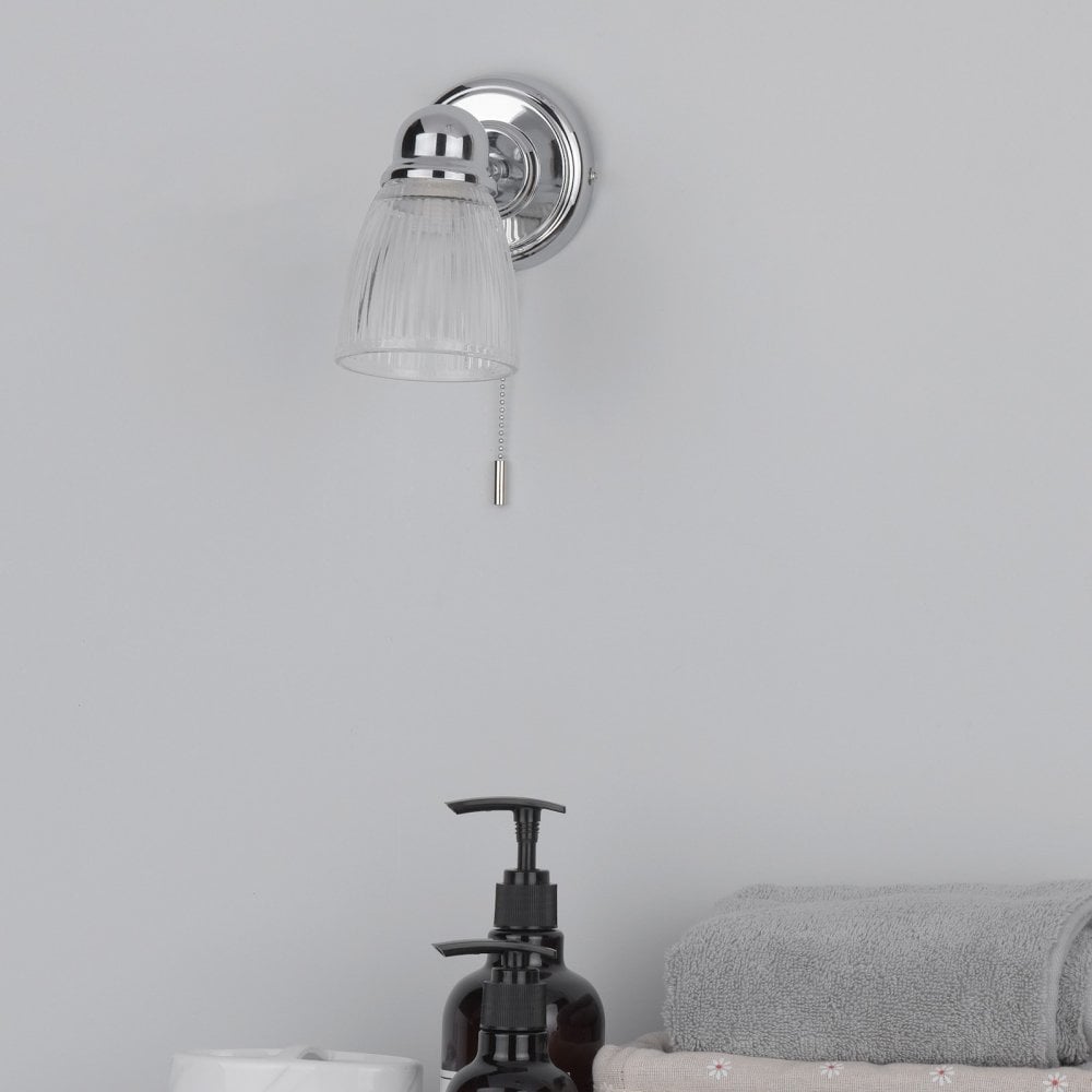 An unlit wall light above a bathroom sink with soap and stacked towels.