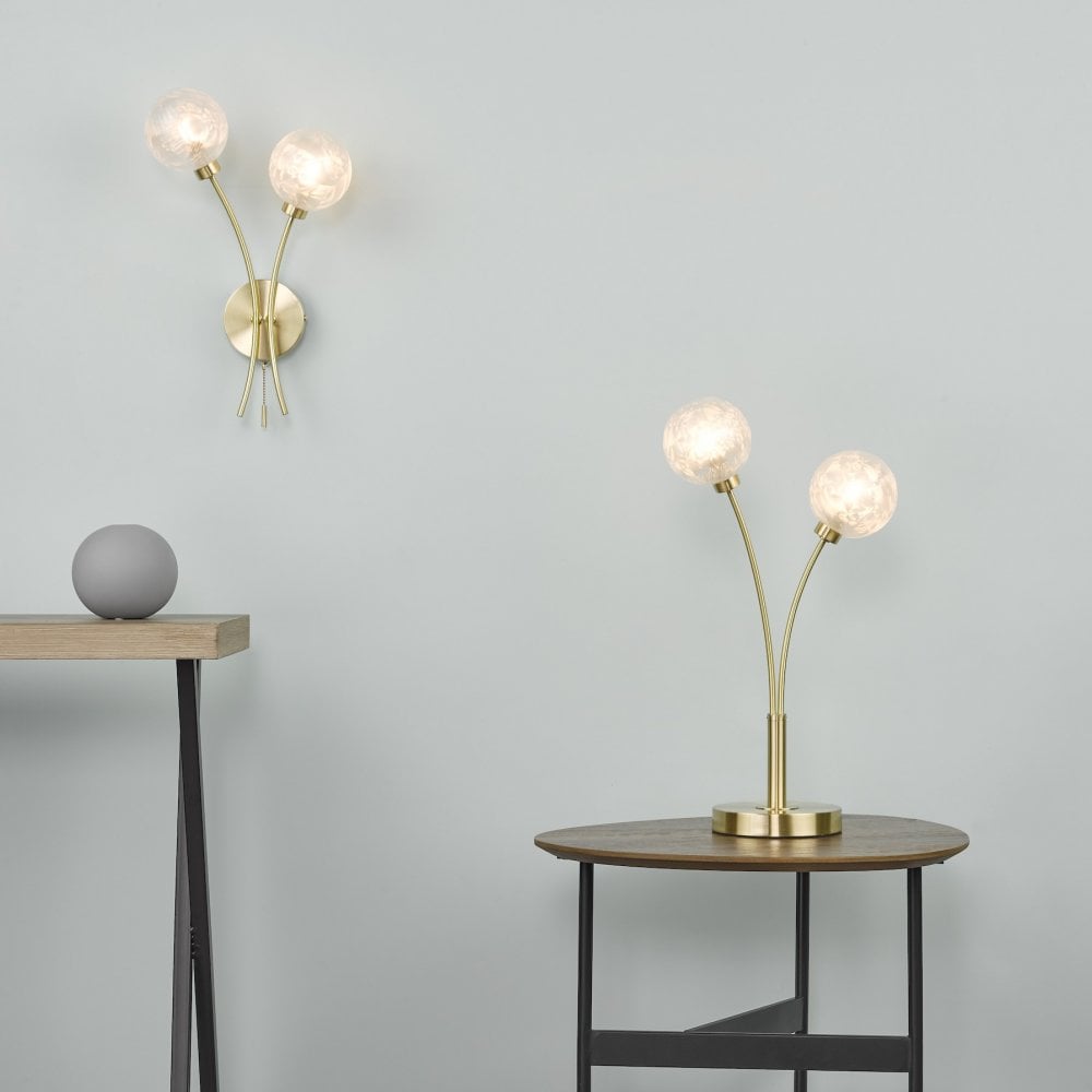 A brass wall light and matching table lamp with spherical glass shades illuminate a room.