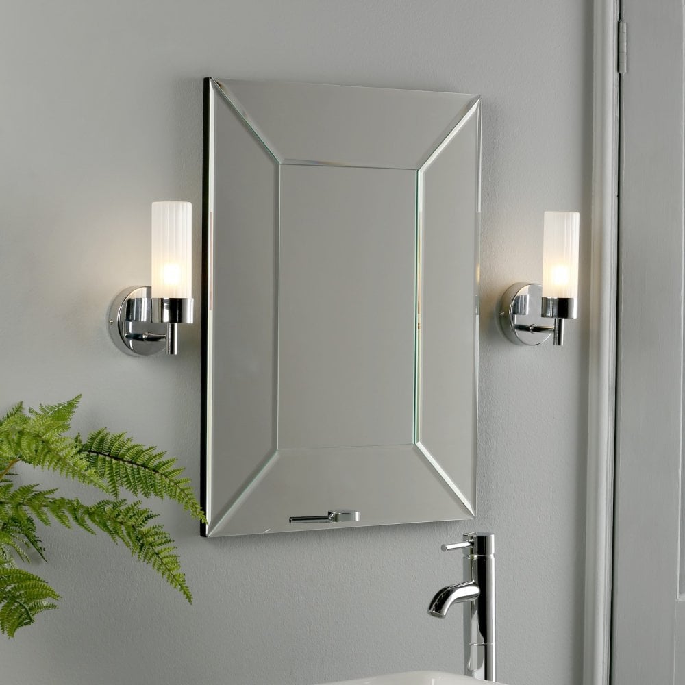 Two bathroom wall lights flank a large mirror above a sink with a faucet.