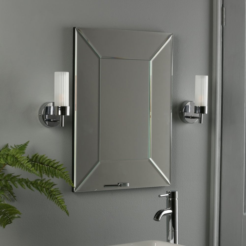 Two wall lights illuminate a framed mirror above a bathroom sink and faucet.